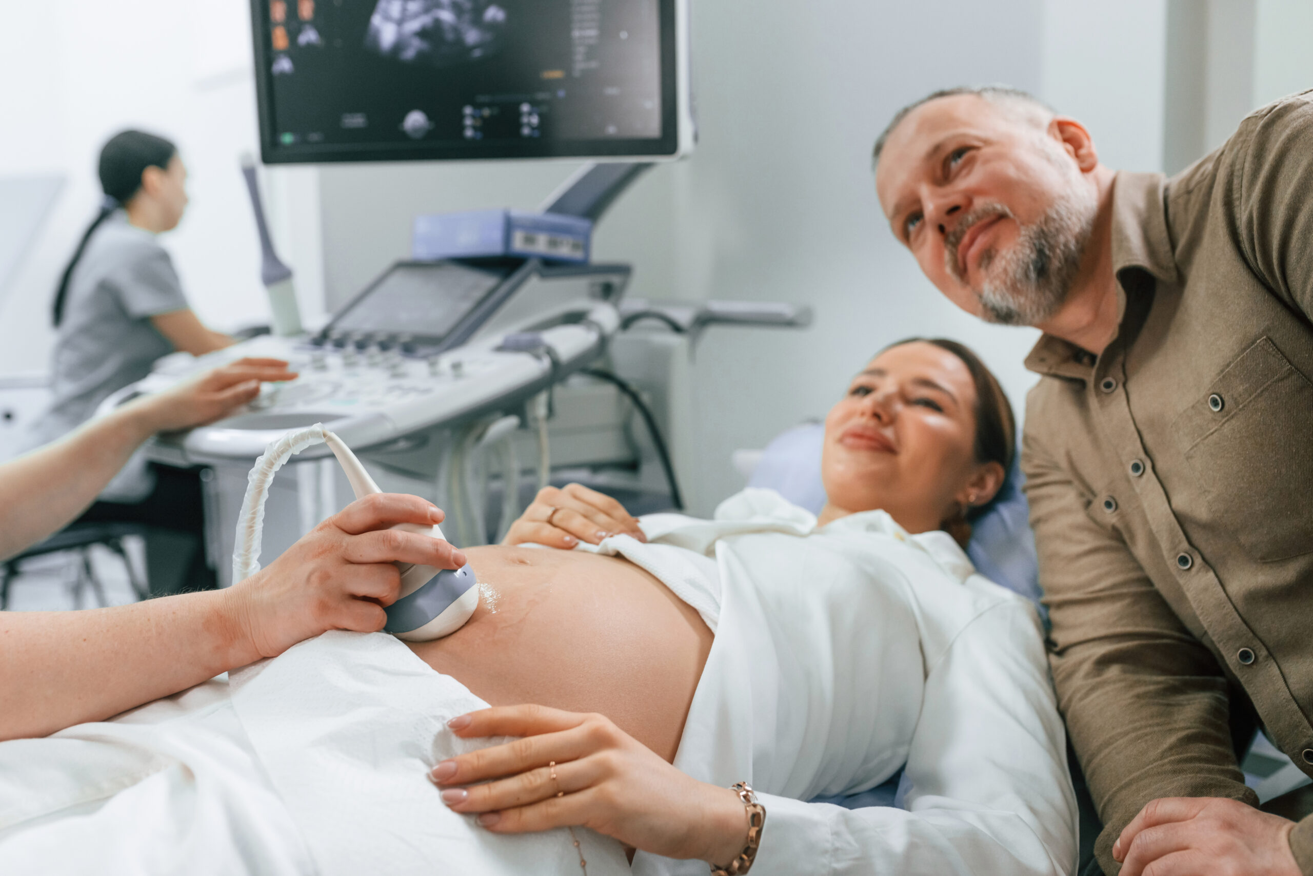Husband is supporting his wife. Pregnant woman is lying down in the hospital, doctor does ultrasound.