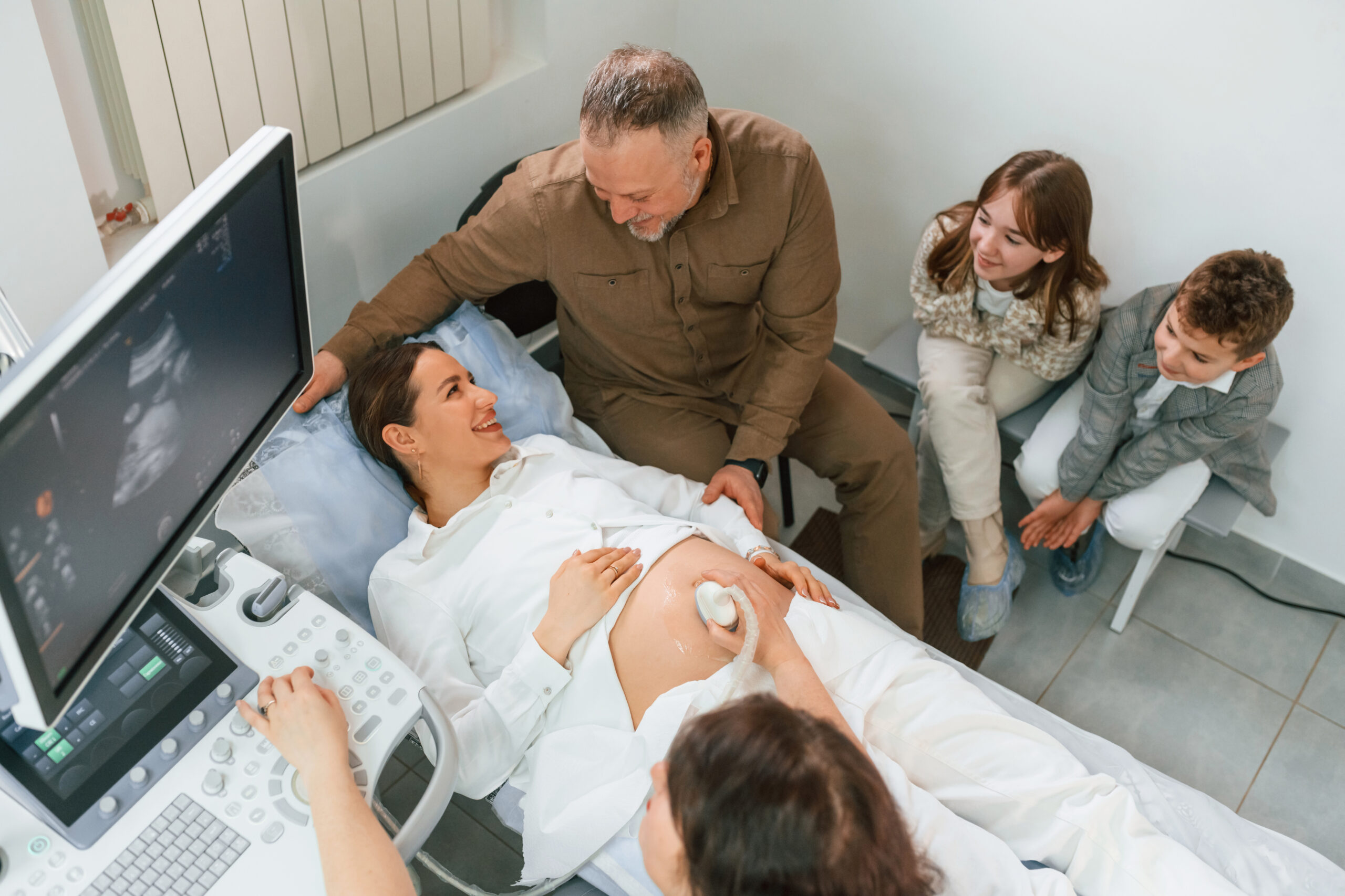Top view. Kids and husband supporting. Pregnant woman is lying down in the hospital, doctor does ultrasound.